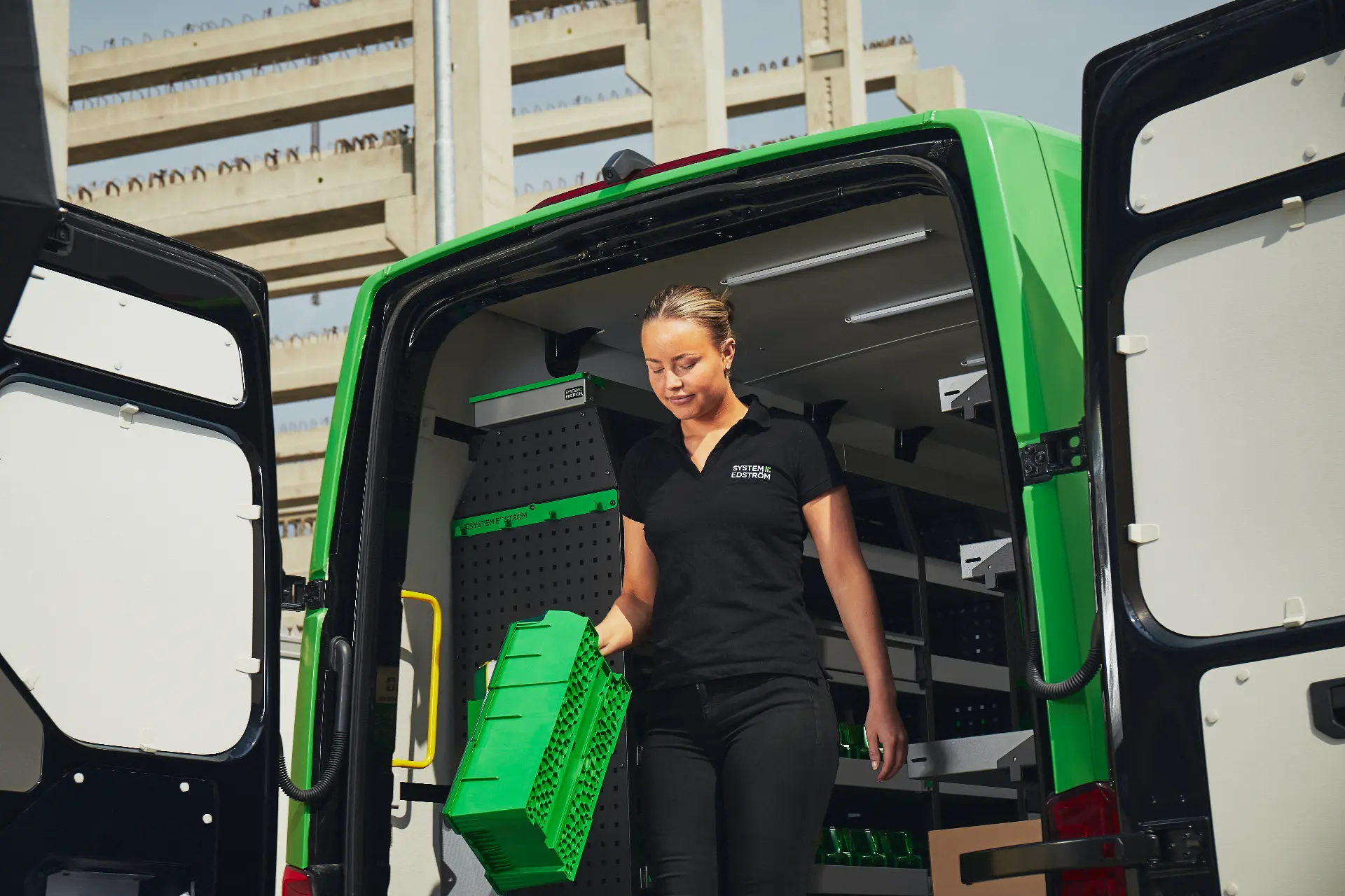 Mitarbeiterin entnimmt eine grüne Transportbox aus dem Laderaum